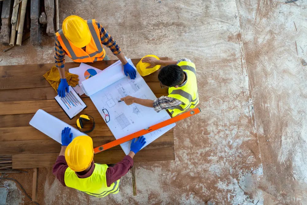 Overhead shot of three construction workers looking at drawings